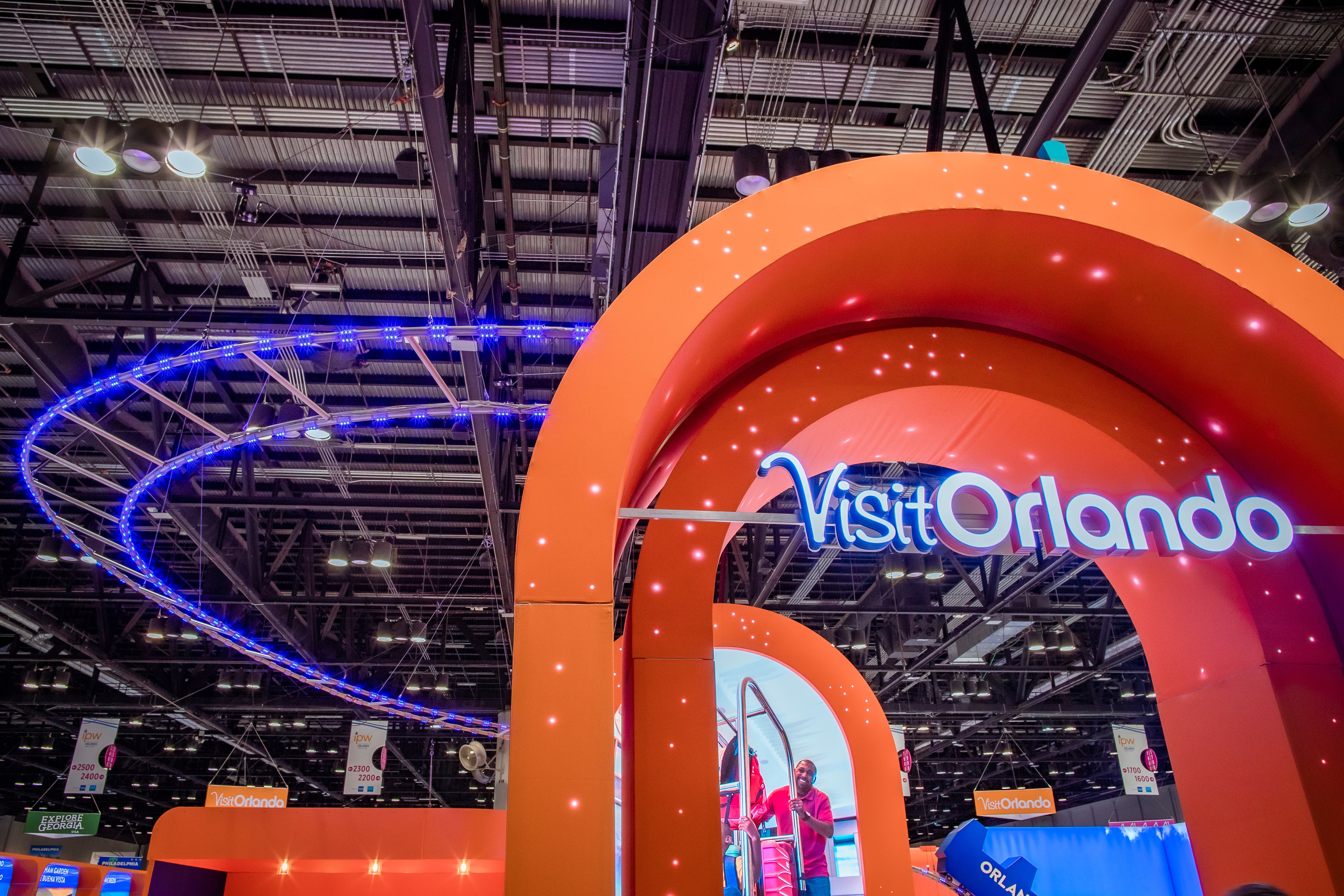 An entryway to the Visit Orlando Booth with an Orange arch and a purple faux coaster track.  There are twinkling stars along the archway. 