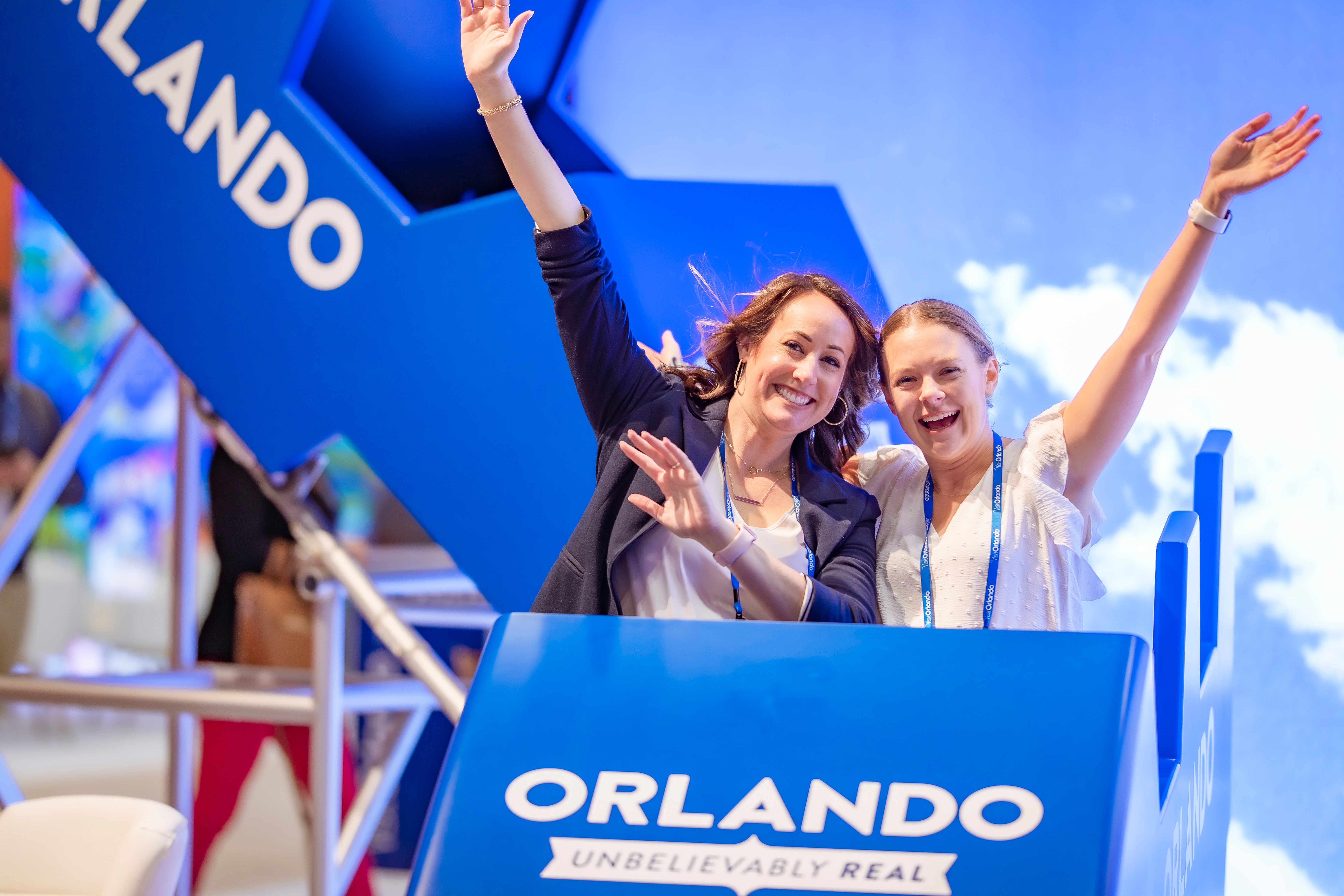 Two black girls, one around 2-4 and the other 8-11 pose together for a photo in front of a light blue LED display. 