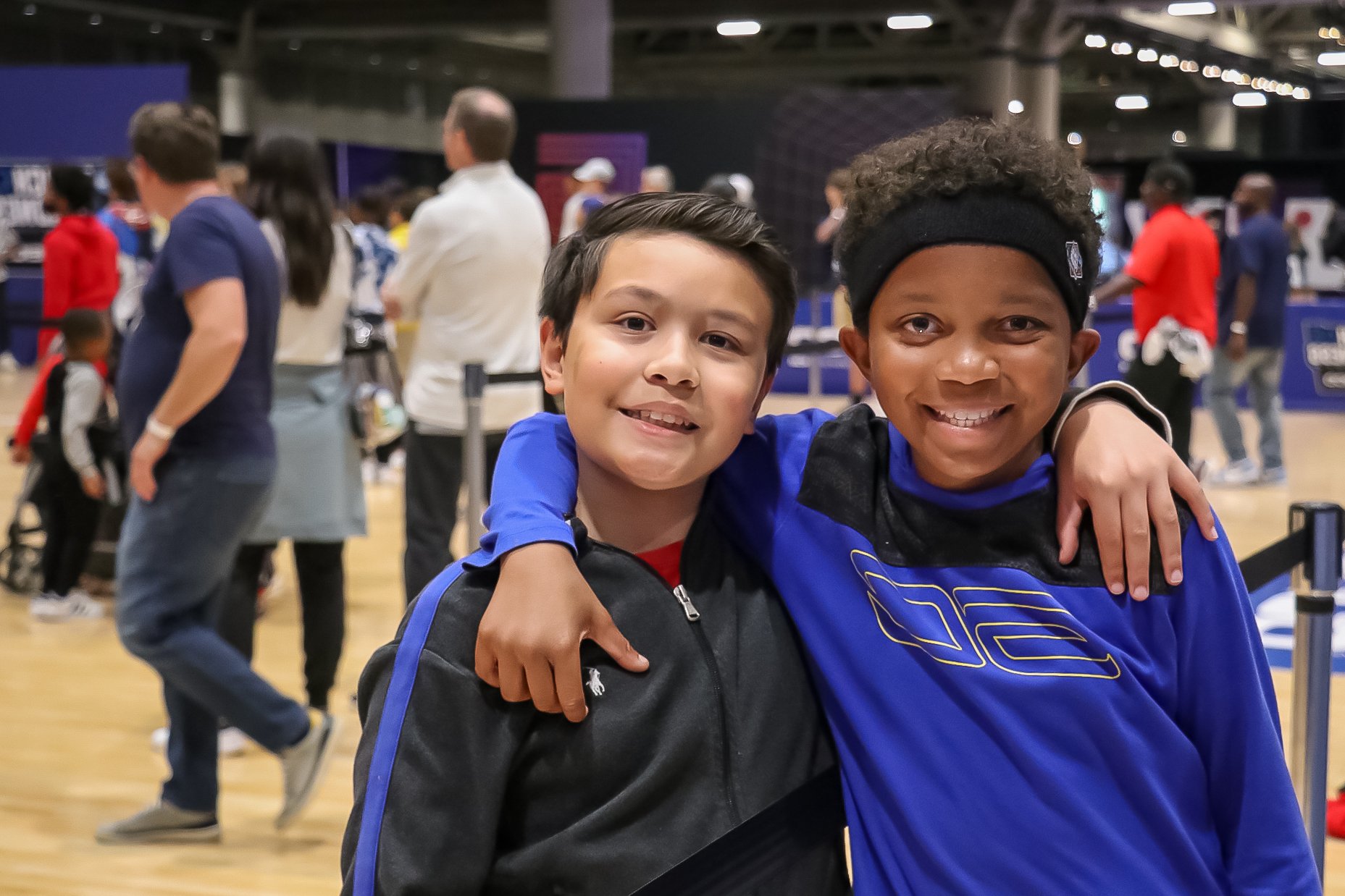 Two child age boys pose for the camera wearing matching athletic gear. The boy on the left is Hispanic while the boy on the left is black