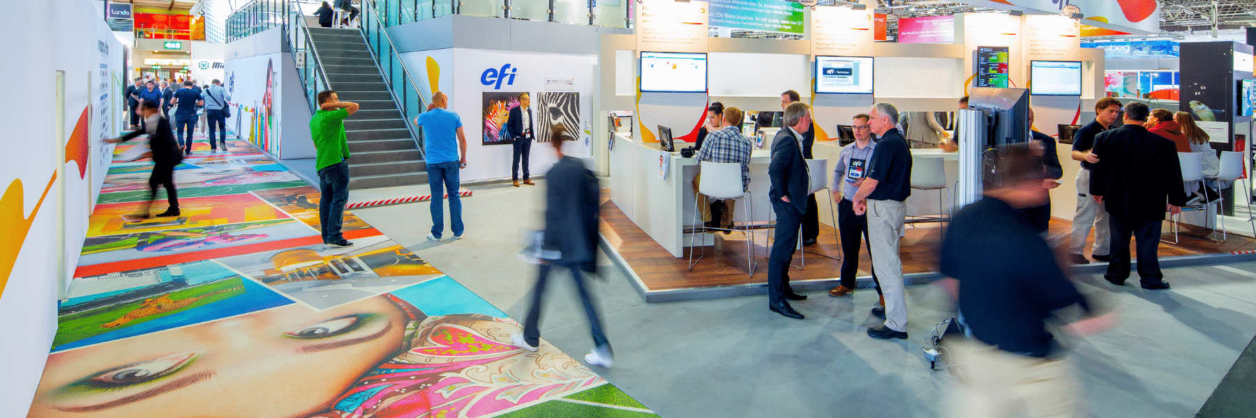 People walking through booths on the EFI Drupa show floor